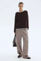 Buzo de punto fino color marrón oscuro, de corte holgado con escote redondo y mangas raglán. Presenta puños y bajo acanalados.