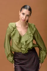 Camisa de color verde oliva con escote en V y volados frontales. Presenta mangas largas con puños elásticos y una textura ligera y sutilmente brillante.