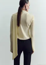 Blusa de manga larga en color crema, confeccionada en poliéster. Presenta un diseño de cuello alto con un sutil detalle de abertura frontal y corte recto.