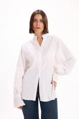 Camisa blanca de corte oversize con textura de rayas verticales sutiles. Presenta cuello mao, cierre frontal con botones y mangas largas abullonadas con puños anchos.