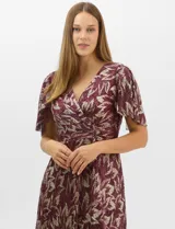 Vestido largo de fiesta con diseño cruzado, escote en V y drapeado lateral en la cintura. Presenta mangas cortas acampanadas y falda amplia con caída fluida. Confeccionado en tejido liviano con acabado plisado y estampado floral metalizado.