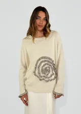 Sweater color crema con aplique de volados grises formando una flor en el frente.