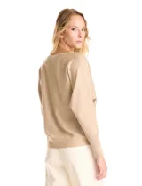 Buzo de tejido fino color beige, con mangas tipo dolman y puños ajustados. Presenta un diseño frontal decorado con apliques de tachas metálicas pequeñas dispuestas en líneas verticales.
