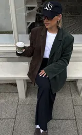 Blazer de gamuza con diseño bitono, presentando un lado en color marrón chocolate y el otro en verde pino. Posee solapas clásicas, cierre frontal con botones y bolsillos laterales funcionales.