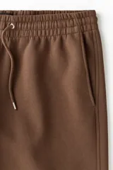 Pantalón deportivo de felpa marrón con elástico en la cintura, cordón de ajuste y bolsillos laterales, corte holgado.