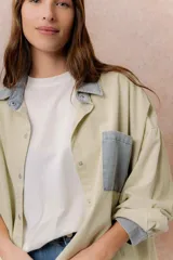 Camisa lila de calce relajado y manga larga, con cuello clásico, puños y bolsillo delantero en denim contrastante. Cierre frontal con broches metálicos.