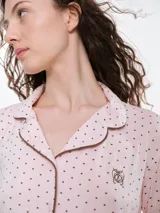 Camisa de pijama de manga larga con cuello solapa y cierre frontal de botones. Presenta un estampado sutil de pequeños corazones sobre una base de color gris melange, con detalles de ribete en contraste en el cuello y la botonera.