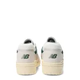Championes New Balance modelo 550, color blanco hueso con detalles en verde oscuro. Presentan un diseño de corte bajo inspirado en el básquet, con paneles de cuero y malla, y el logo 'N' en verde oscuro. La suela es de goma color crema.