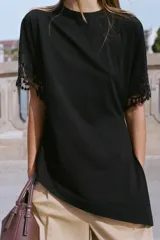 Camiseta negra de algodón con cuello redondo, manga corta y detalle de aplicación de encaje a tono en los puños. Presenta un diseño con bajo asimétrico y frunce lateral.