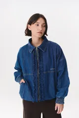 Campera de denim azul con corte oversized, cierre frontal y cuello de piel sintética marrón desmontable. Presenta detalles de volados en el frente, puños elásticos y logo bordado en el pecho.