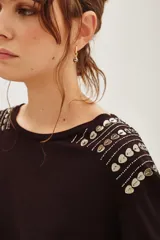 Remera de viscosa color negro, con cuello redondo y mangas cortas. Presenta un detalle decorativo de apliques metálicos en forma de corazón dispuestos en líneas sobre los hombros.