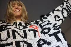 Sweater tejido a mano en 100% algodón, con diseño geométrico en blanco, negro, naranja y rosa. Corte holgado y flecos en el ruedo.