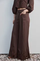 Pantalón largo negro de corte ancho y holgado, con bolsillos laterales y detalle de bordado calado en el ruedo.