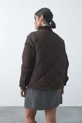 Campera tipo barn capitoneada de color marrón, con silueta corta y relajada. Presenta cuello de pana, cierre frontal con broches metálicos y bolsillos laterales funcionales.