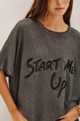 Remera de corte holgado y mangas cortas, confeccionada en tejido gris con efecto lavado. Presenta una estampa frontal con la frase 'Start Me Up' realizada en lentejuelas negras.