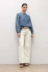 Camisa de jean azul con mangas largas abullonadas, puños elásticos y cuello redondo mao. Cuenta con cierre frontal de botones ocultos.