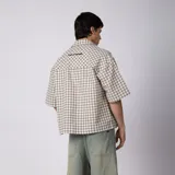Camisa de manga corta de popelina con patrón a cuadros, calce boxy y largo a la cintura, con bolsillos y canesú cortados en diagonal.