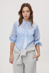 Camisa de manga larga con diseño de rayas verticales en tonos celestes, blancos y marrones, confeccionada en tejido semitransparente con cuello camisero y cierre frontal de botones.