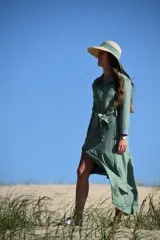 Vestido camisero largo de color verde, con cuello clásico, cierre frontal de botones y lazo ajustable en la cintura. Presenta mangas largas con puños y una falda con abertura lateral.