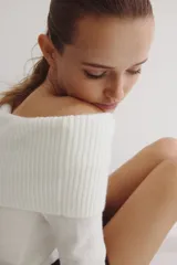 Buzo corto de punto suave color blanco, con escote off-the-shoulder con doblez ancho acanalado. Tiene remate acanalado en puños y bajo.