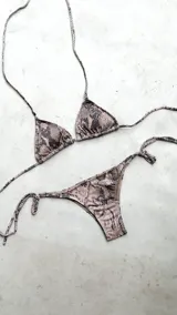 Bikini con estampado animal print de serpiente en tonos rosados y negros. El top es de triángulos movibles con tiras para atar al cuello y espalda, e incluye almohadillas desmontables. El bottom es una vedetina con tiras ajustables a los costados para atar a la medida de la cadera.