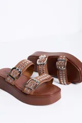 Sandalias de plataforma color marrón camel, con dos tiras en el empeine decoradas con hebillas metálicas plateadas y tachas. Suela plana y corrida.