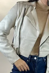 Chaqueta corta tipo biker confeccionada en gamuza color beige, con cierre frontal cruzado, solapas amplias, bolsillos con cierre y cinturón ajustable en la cintura.