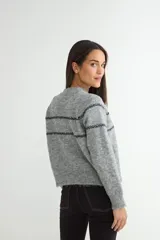 Cardigan de punto gris con cierre frontal de botones oscuros. Presenta un diseño de rayas horizontales oscuras y pequeños bordados florales en la parte superior del pecho y mangas.