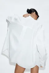 Camisa oversize de cuello solapa, manga larga con hombro caído y puños con pliegues. Presenta un bolsillo de plastrón en el frente, detalle de pinza con trabilla y botón en la espalda, bajo asimétrico y cierre frontal con botones.