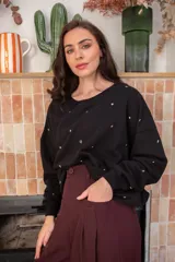 Sweater de corte oversize color beige, confeccionado en algodón. Presenta un diseño holgado con cuello redondo, puños y ruedo acanalados, decorado con múltiples apliques metálicos circulares en tonos dorados y plateados distribuidos por toda la prenda.