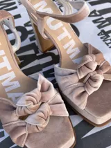 Sandalias de tacón alto Mutma modelo Ñoma, confeccionadas completamente en terciopelo color verde militar. Presentan una plataforma delantera, detalle de doble nudo o moña en la puntera, taco ancho y tira con hebilla ajustable en el tobillo.
