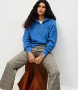 Suéter de punto azul con cuello alto y cierre frontal de cremallera metálica. Presenta textura de líneas verticales, corte regular, mangas largas y terminaciones acanaladas.