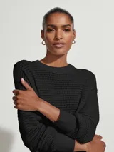 Sweater negro de punto con textura tipo waffle, cuello redondo y mangas largas con puños acanalados.