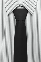 Camisa oversize de popelín a rayas verticales blancas y negras, con cuello solapa, hombros caídos y puños anchos. Incluye una corbata negra lisa.