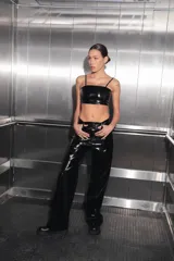 Pantalón de tiro medio-alto confeccionado en charol negro, con diseño de cinco bolsillos, cierre frontal con botón metálico y corte recto.