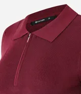 Blusa polo de punto color mostaza, ajustada al cuerpo, con cuello y manga corta. Presenta una cremallera frontal que llega hasta el escote.