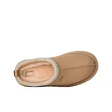 Zuecos UGG modelo Tazz de gamuza color beige, con plataforma alta y detalle de costura trenzada en el borde superior. Presenta el logo de la marca grabado en el lateral.
