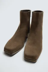 Bota corta color marrón de piel con acabado serraje, cierre de cremallera lateral, horma cuadrada y tacón de 5 cm.