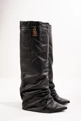 Botas de caña alta color negro, confeccionadas en cuero vegano. Presentan punta fina, caña arrugada y detalle de hebilla dorada en la parte superior.