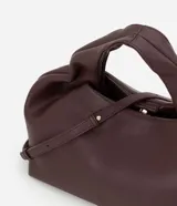 Cartera mediana de diseño estructurado en color bordó, confeccionada en poliuretano con acabado liso. Presenta asas de mano integradas con detalle fruncido, correa larga ajustable y desmontable, y cierre superior con cremallera.