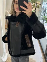 Campera tipo gamulán de cuero genuino en color negro, con interior y detalles de cuello en piel sintética negra. Presenta detalles en estampado animal print de leopardo en los bolsillos laterales y en la solapa. Cuenta con cierre frontal metálico y diseño de corte ajustado.