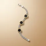 Pulsera de malla tejida en plata, con tres dijes circulares de ónix negro enmarcados en oro amarillo con detalles estriados.