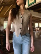 Chaleco color beige con escote en V y cierre frontal con botones. Presenta un bolsillo de parche en el pecho y corte al cuerpo.