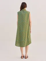 Vestido midi camisero sin mangas, de corte recto y holgado. Cuenta con cuello camisero liso en color naranja y cierre frontal parcial con botones. Presenta un estampado geométrico psicodélico en tonos naranja y beige.