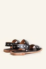 Sandalia baja de cuero vacuno color negro con acabado efecto charol texturizado, decorada con tachas metálicas plateadas en las tiras y la sujección del talón. Cuenta con suela plana de cuero.