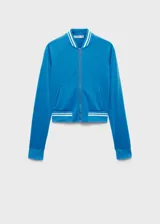 Chaqueta tipo bomber color turquesa con cierre frontal de cremallera, cuello redondo y puños con detalles de rayas blancas en contraste. Presenta un diseño recto con dos bolsillos laterales.