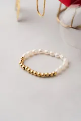 Pulsera elástica con cuentas de perlas blancas y cuentas doradas.