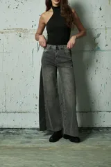 Jean de corte wide leg en color gris lavado, con diseño bicolor que presenta un panel lateral en un tono de gris más oscuro. Posee tiro medio, cierre frontal con botón y bolsillos laterales.