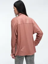 Camisa de corte oversize confeccionada en tejido jersey con acabado brillante. Presenta cuello en punta, cierre frontal con botones, mangas largas con puños anchos y tajos laterales en el ruedo.