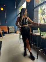 Pollera midi negra de cuero sintético con abertura frontal y flecos largos en el ruedo. Se combina con un crop top haciendo juego y botas de caña baja.